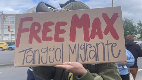 Close-up of a person holding a cardboard protest sign reading “FREE MAX” in large red letters, with “Tanggol Migrante” written below in black.