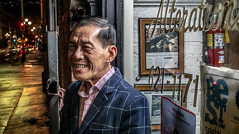 Be Van Nguyen stands smiling outside his Seattle alterations shop in Pioneer Square, with reflections of awards and press clippings in the window.