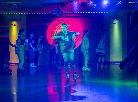 A skater dances to music in dim lighting while others skate around them.