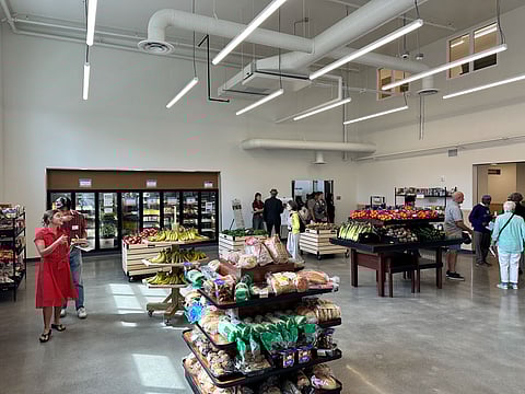 The interior of the Rainier Valley Food Bank, with bread and produce stands throughout an open space and people walking through and shopping.