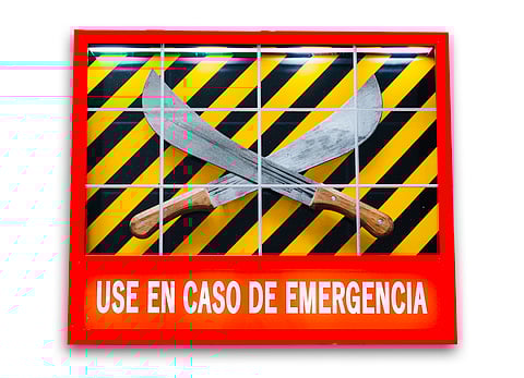 An artwork reads "Use en caso de emergencia" and looks like an emergency sign; two hatchets are crossed at the center of the artwork.