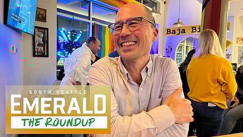 Eddie Lin is smiling and leaning on his arms that are resting atop a table. He's wearing a button-down shirt and glasses. 