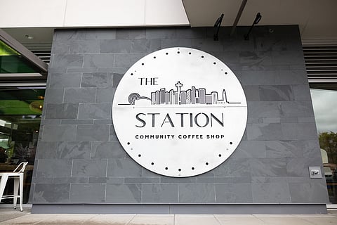 Exterior sign for The Station community coffee shop in Columbia City, featuring a circular logo with a city skyline design.