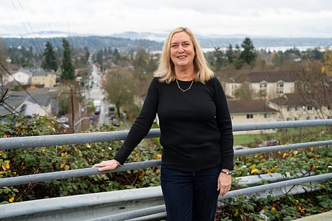 A female figure, with shoulder-length blonde hair and wearing a black sweater and pants, leans against a gray railing.
