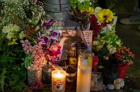 Roadside memorial with lit candles, flower bouquets, and a laminated photo honoring a cyclist killed in a hit-and-run at Beacon Avenue South and South Stevens Street.