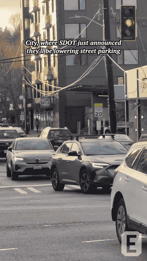 Cars drive through a busy city intersection with a traffic light and apartment buildings in the background.