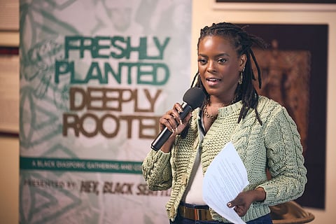 A Black woman with braids and wearing a light-green cardigan speaks into a mic.