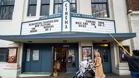 A staff member uses a long pole to change letters on the Tasveer Film Center marquee while a woman pushes a stroller past the entrance of the building.
