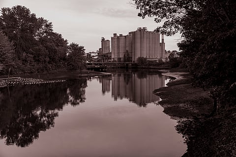 A red-sepia toned image shows the smooth surface of the Duwamish River with a large, industrial building in the background.