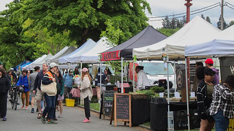 Crowds browse vendor tents at Columbia City Farmers Market in Seattle under grey skies.