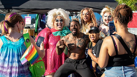 People pose for photos with drag performers in colorful costumes and makeup at an LGBTQ+ Pride festival celebration.