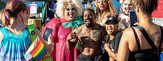 People pose for photos with drag performers in colorful costumes and makeup at an LGBTQ+ Pride festival celebration.
