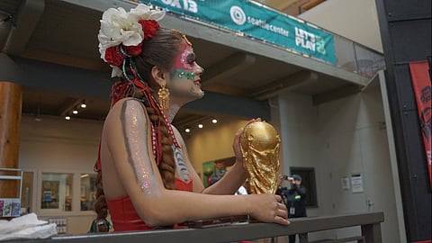 A woman holds a World Cup statue in her hands, and she's dressed in the Mexican team's colors, with paint and glitter on her arms and face and large red and white flowers in her hair.
