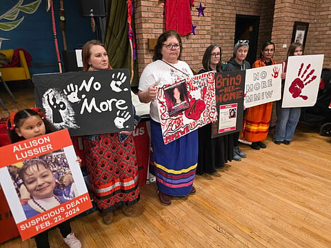 Several women and a young child hold posters that identify missing and murdered Indigenous women and girls.