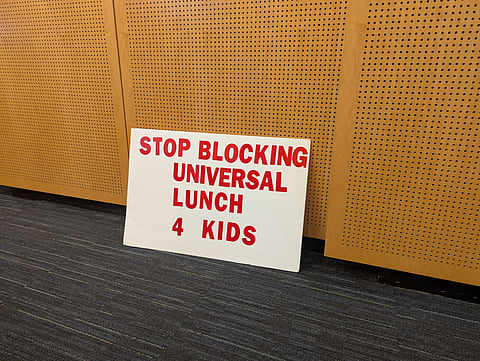 Sign on City Hall floor reads "Stop blocking universal lunch 4 kids."