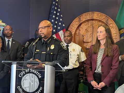 Seattle Police Chief Shon Barnes talks at a podium while others, including King County Exec. Girmay Zahilay and Seattle Mayor Katie Wilson look on.