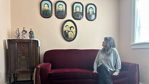 Sue May Eng looks up at photos of her grandparents and great-grandparents in the historic Eng Family Home in August 2026. 