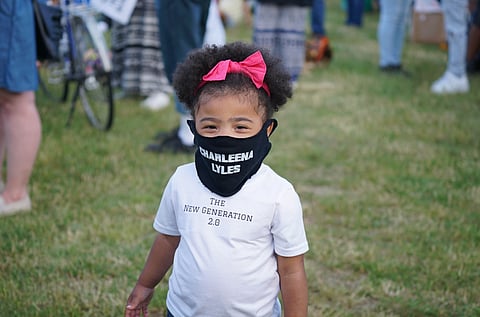 A young child wears a Charleena Lyles face-covering at Seattle's Magnuson Park for a June 18 Remembrance Vigil in honor of Charleena Lyles, on the third anniversary of her death at the hands of two Seattle police officers. The apartment she lived in with her four children when she was killed in 2017 is just a few hundred yards from where the crowd gathered to pay their respects, listen to friends and family speak about Charleena and to celebrate her life. (Photo: Susan Fried) 
