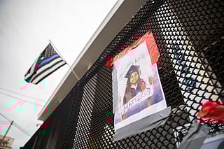 A poster attached to a fence reads "JAAHNAVI'S LIFE MATTERED," with an image of Jaahnavi Kandula wearing a graduation cap, commemorating her life. Above the poster, a thin-blue-line flag flies above the Seattle Police Officers Guild building.