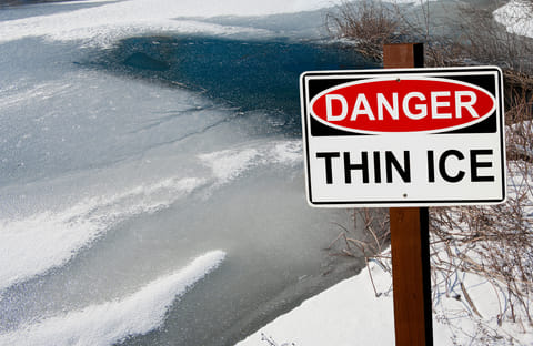 A thin ice warning sign in front of a frozen pond. 