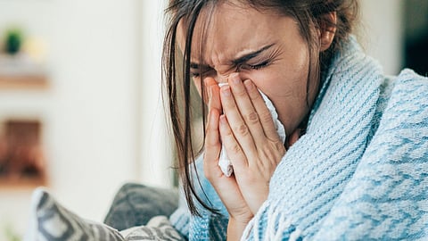 A young women wrapped in a blanket blowing her nose. 