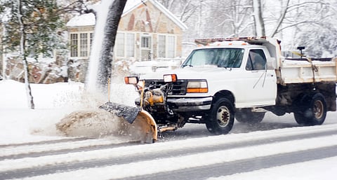 White truck with a yellow snow plow attached to the front pushes snow along a suburban neighborhood street. Hanover Select Board discusses snow removal budget shortfall and potential funding solutions.