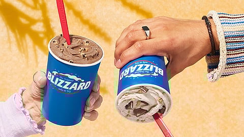 Two hands hold Dairy Queen blizzards, one holds it upside down. 