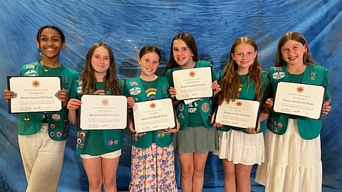 Six Girl Scouts wearing their green vests hold their Bronze Award certificates.