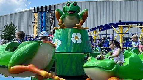 Children ride the Frog Jump which is a ride with one frog on a lily pad in the middle and frogs for kids to ride in around it in a circle 