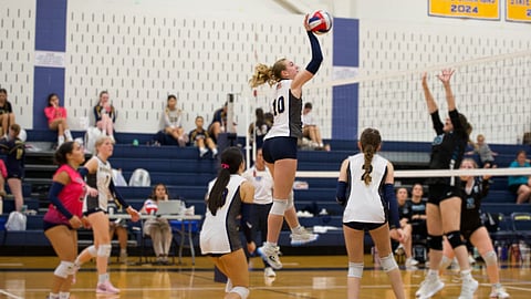 Girls playing volleyball inside of a gym. 