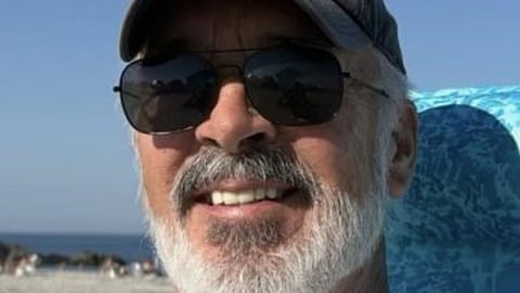 The face of a man with a white beard wearing sunglasses and a gray baseball cap.
