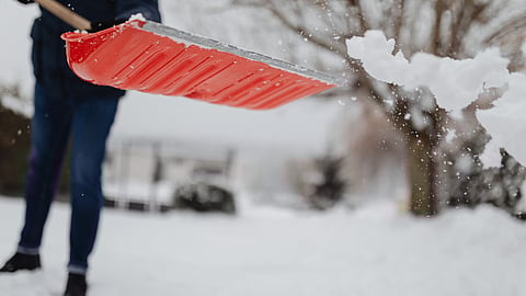 a person shoveling the snow with a red shovel