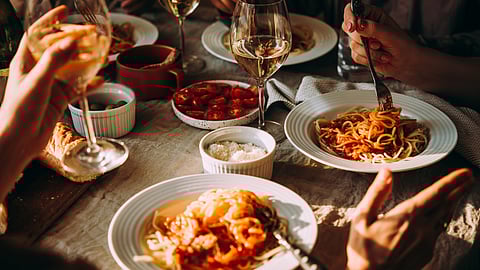 a dinner table with wine glasses, white bowls of pasta and a dish of roasted tomatoes