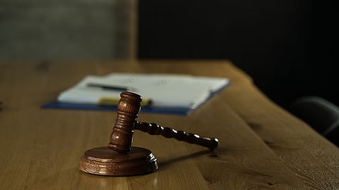 wooden gavel on a wooden desk next to a folio of papers and a pen