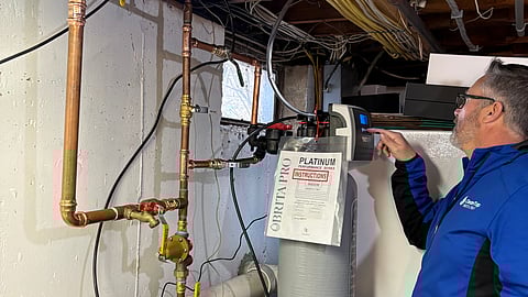 a man wearing a blue zip up jacket is in a basement looking at a water filtration system 