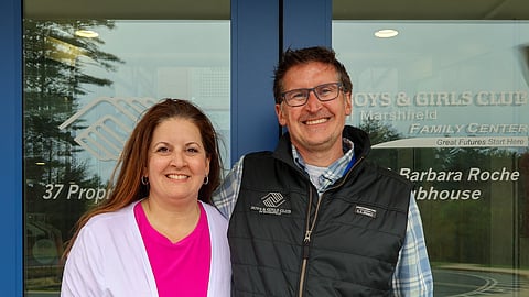 A man and woman pose in front of the doors of the Marshfield Boys & Girls Club building 
