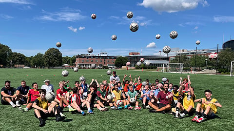 Athletes training at BC High summer sports camp throwing up soccer balls in the air with the red brick school in the background