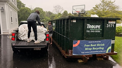 a teenager leans over a truck bed that has a lot of plastic wrap in it next to a dumpster
