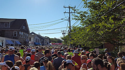 a large crowd of runners stand at the start line of a. road race