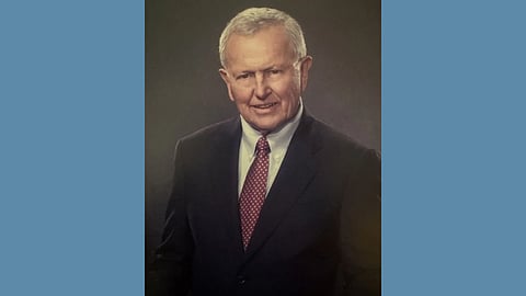 photo of an older white man with silver hair in a sport coat and burgundy tie smiling at the camera against a neutral colored backdrop