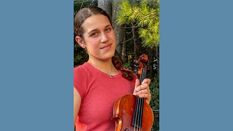 Violinist Anabella Massaro, who will perform with Firebird Pops at South Shore Conservatory in Hingham poses with her violin wearing a red shirt 