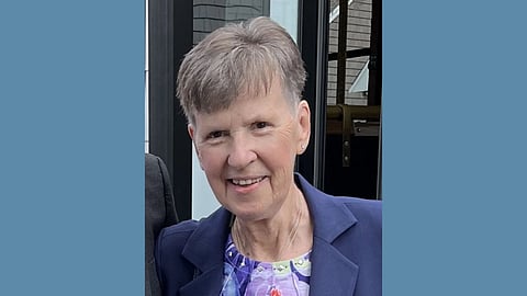 Photo of an older white woman with short grey hair wearing a purple floral top and navy blazer, smiling warmly 