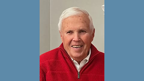 Elderly white man with white hair wearing a red zip up sweater and smiling 
