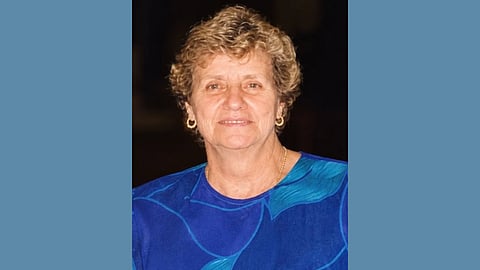 Older white woman wearing a cobalt blue top and small gold hoop earrings smiles at the camera