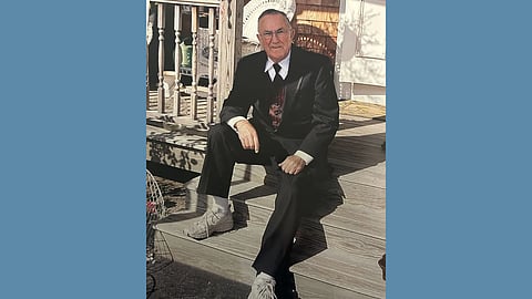 Older white man in a tuxedo and sneakers sits on a set of wooden stairs