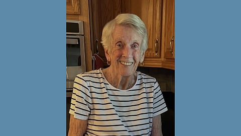 Elderly white woman with short white hair wearing a white and black striped top smiles at the camera 