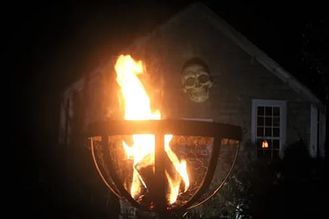 A open flame burns in a basket with a skeleton home decoration in the background
