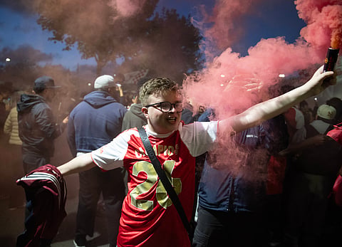 A young Arsenal fan holds a flare and wearing the Champions tshirt outside Emirates Stadium