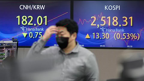 A currency trader passes by the screens showing the Korea Composite Stock Price Index (KOSPI), right, at the foreign exchange dealing room of the KEB Hana Bank headquarters in Seoul, South Korea, Dec. 4, 2023.