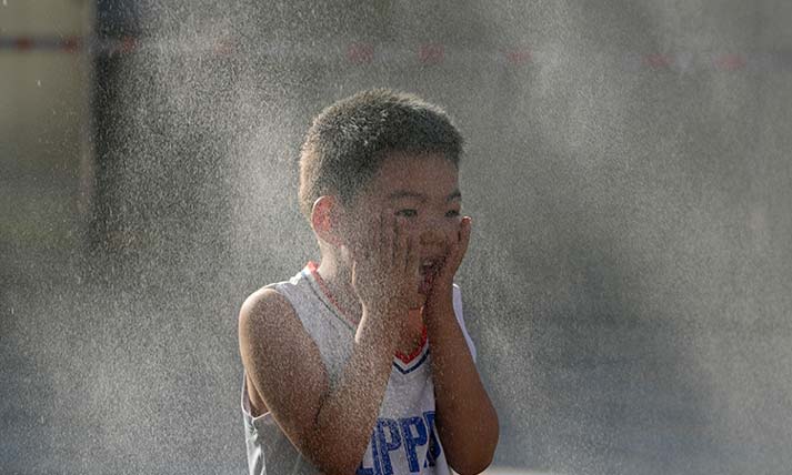 A child reacts to a mist machine as he cools off from the summer heat in Beijing, Saturday, June 15, 2024. 
